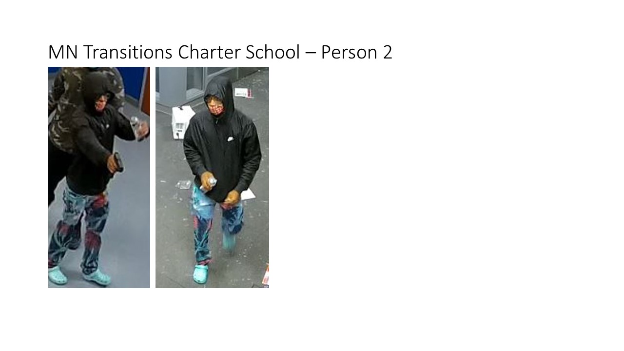 A man in a black hooded wind jacket with light blue Crocs and painted jeans.