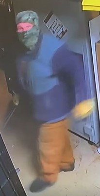 Person standing with face covered and object in hand