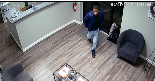 A person in a blue jacket, blue jeans, and black shoes entering a building at 4:18am on 01/01/2023.