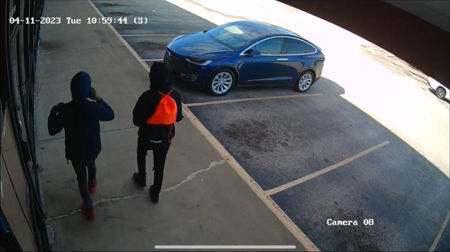 Two people with dark-colored clothing with their hoods up. One person has a bright orange backpack.