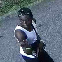 The alleged suspect standing outside and wearing a white tank top.