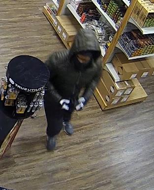 A person in a hooded jacket, mask and gloves in a store.