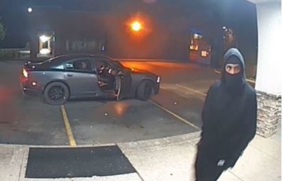 A person in black colored clothing near a car with an open passenger door.