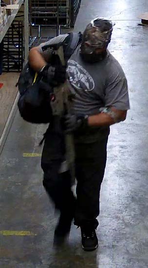 A man with a backpack and wearing a mask, holding a long item, walking inside a building.