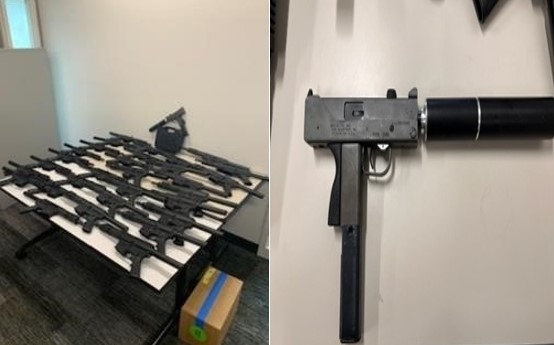 Multiple guns laying on a table and an automatic weapon with a silencer on it