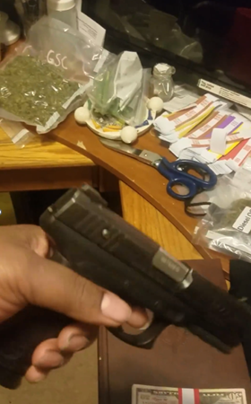 Suspect holding gun with money and suspected drugs laying on table