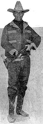 Tom Threepersons holding a rifle and carrying a holstered pistol